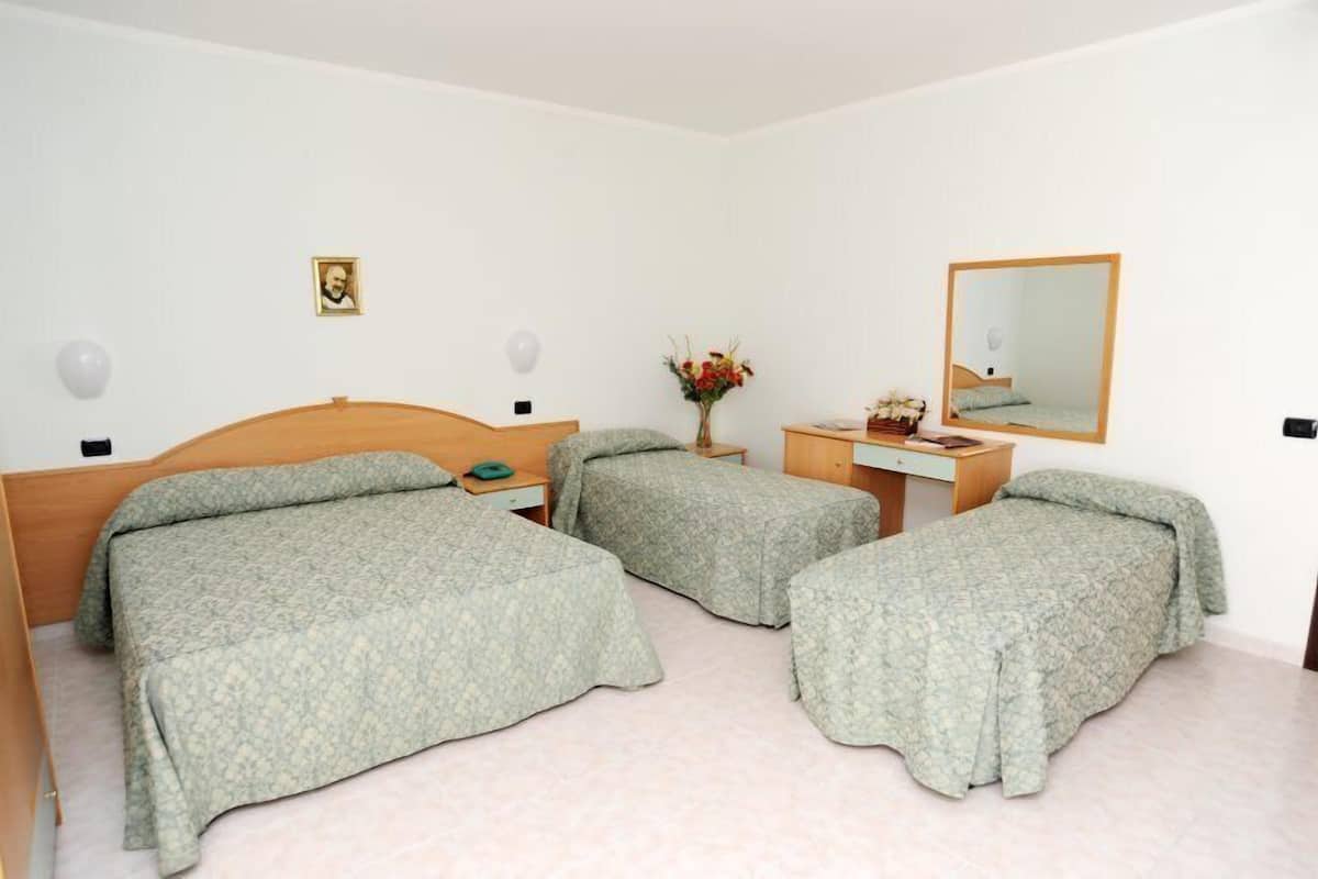 A room with two single beds, a wooden dresser, a mirror, and a small table with a vase of flowers.
