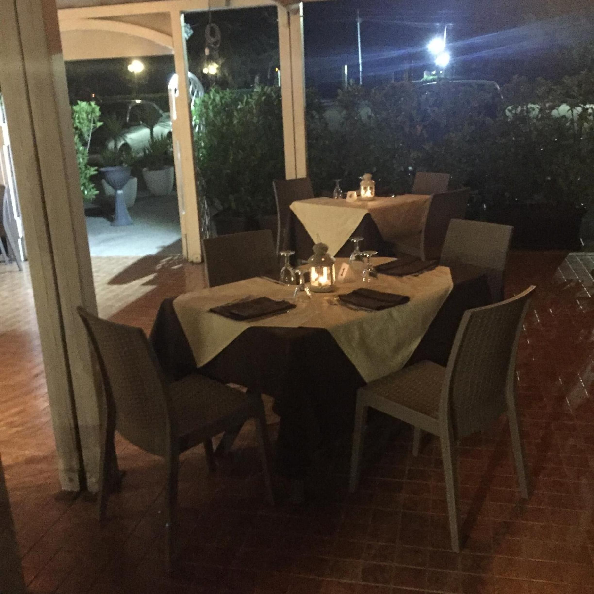 An outdoor dining area with tables set for two, chairs, and a small table with a candle.