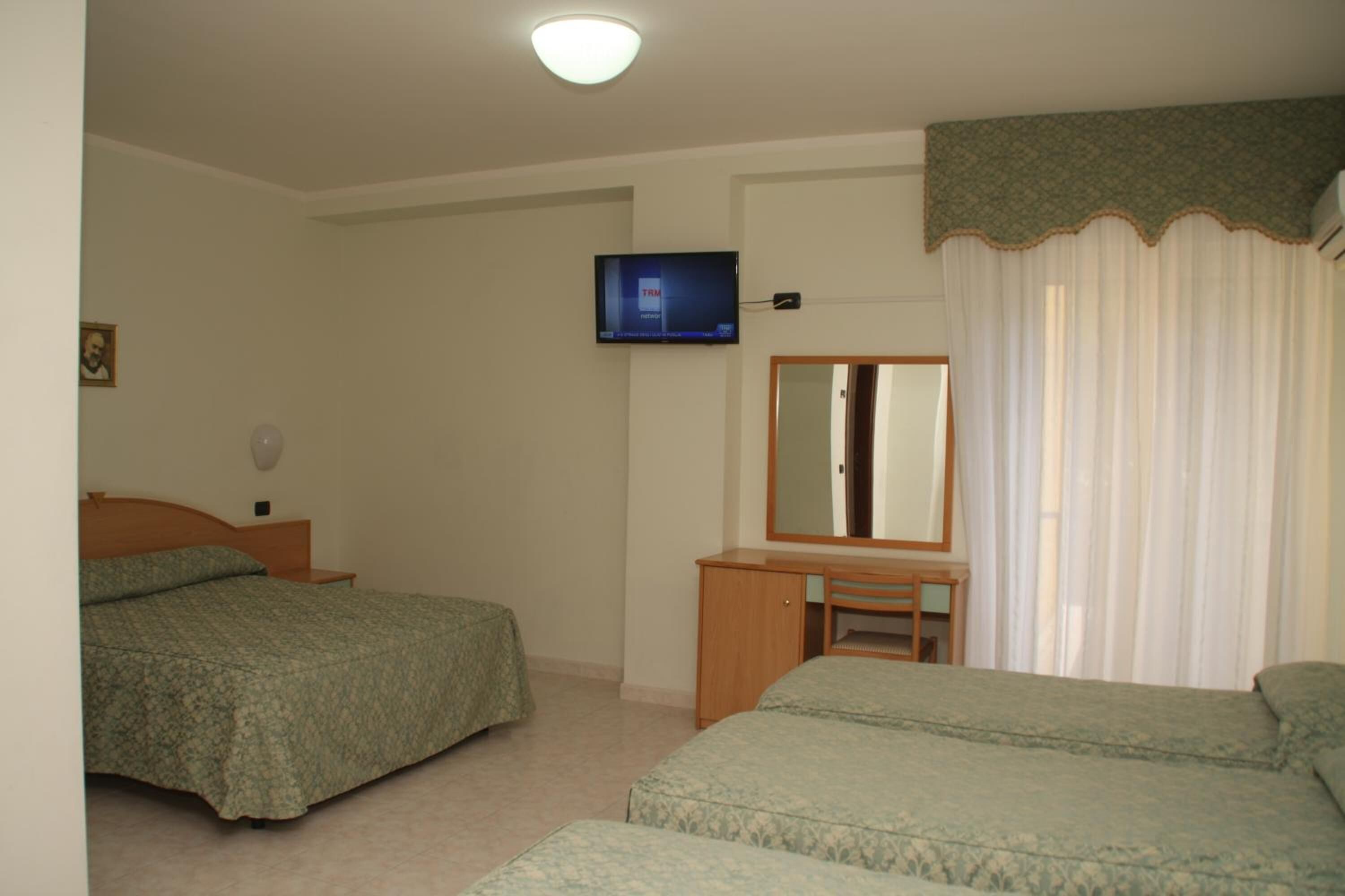 Una camera da letto con due letti, una TV a parete, una scrivania e uno specchio.