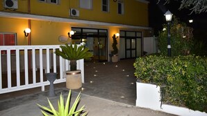 A yellow building with a white fence, potted plants, and a well-lit entrance. - Hotel Garden (San Giovanni Rotondo)