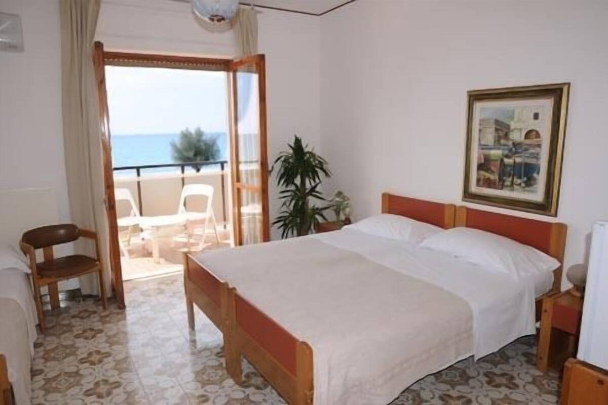 Una habitación de hotel con cama, una silla, una mesa, una planta en maceta y un cuadro en la pared.