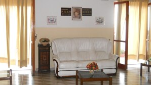 A living room with a white sofa, a wooden coffee table with a vase of flowers, and two framed pictures on the wall. - Hotel Harmony (Tortora)