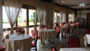 A restaurant with round tables, red chairs, and large windows with curtains. - Hotel Harmony (Tortora)