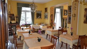 A dining area with multiple tables and chairs, a chandelier, and various framed artworks on the walls. - Hotel Villa Ruscello (Baveno)