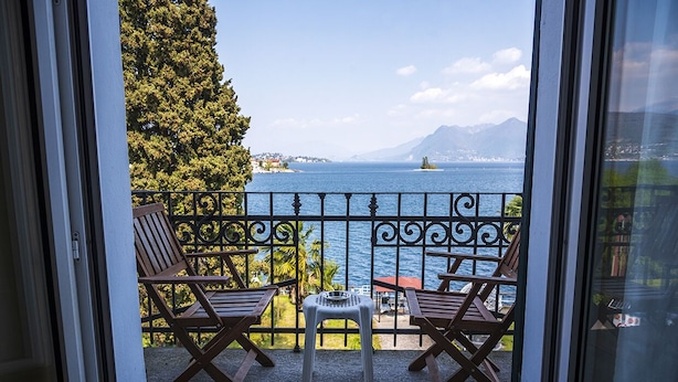 A balcony with two wooden chairs and a small table, overlooking a body of water and distant mountains. - Hotel Villa Ruscello (Baveno)