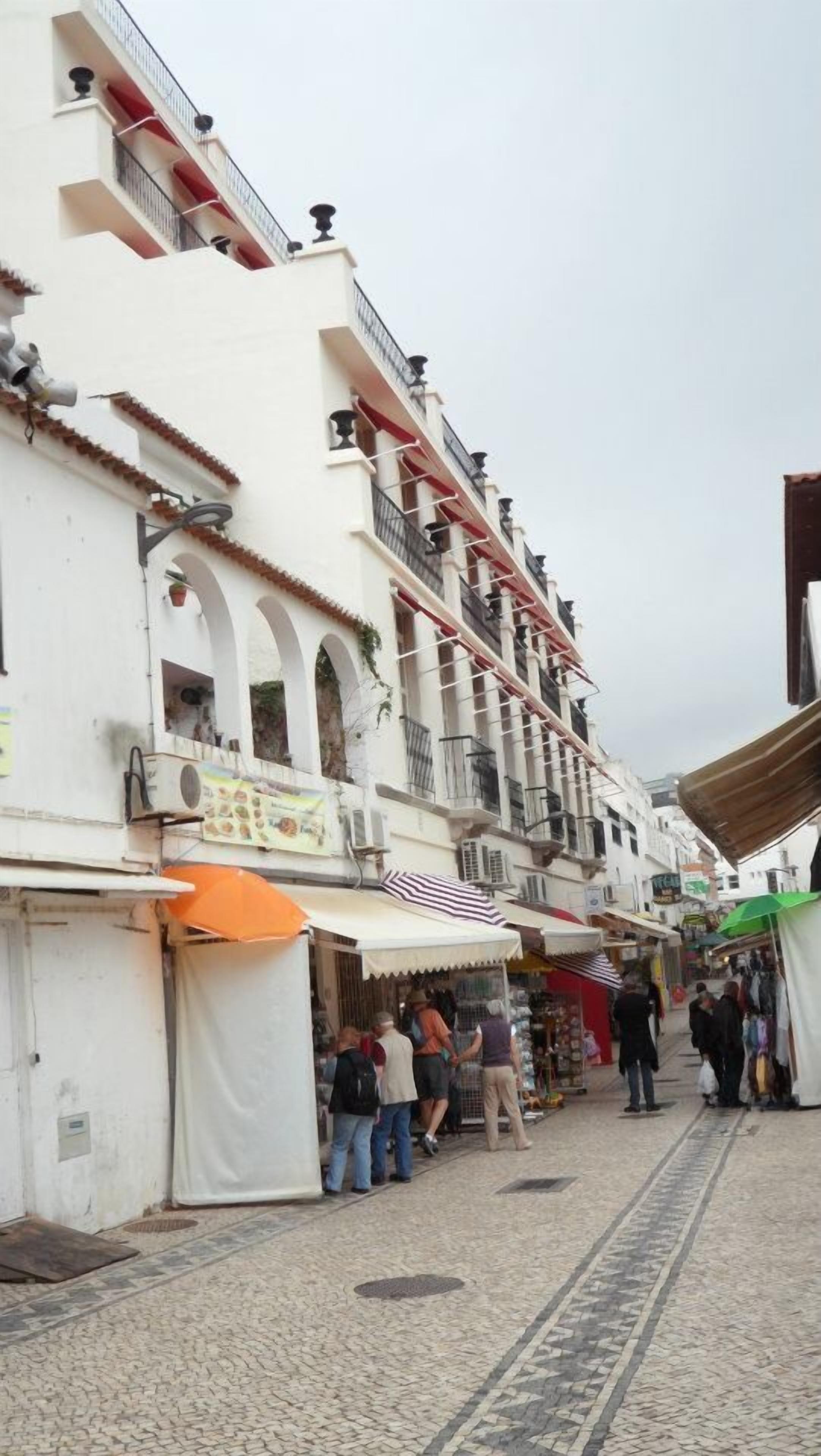 A street with white buildings, balconies, and shops.