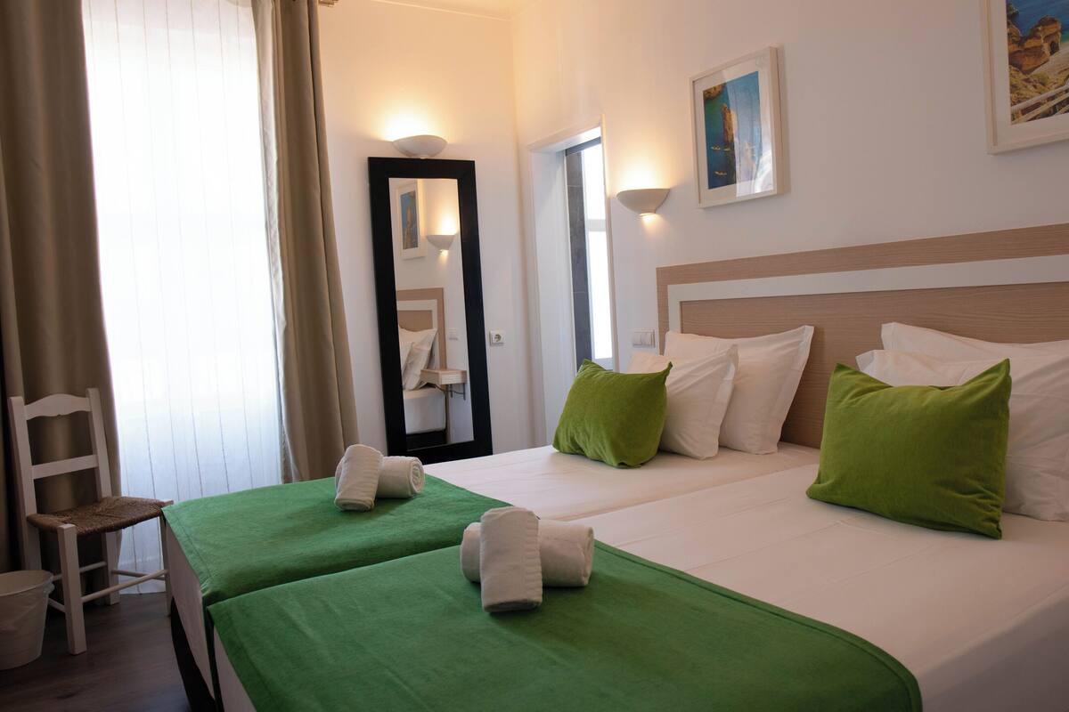 A hotel room with two beds, green bedspreads, white linens, and a wooden headboard.