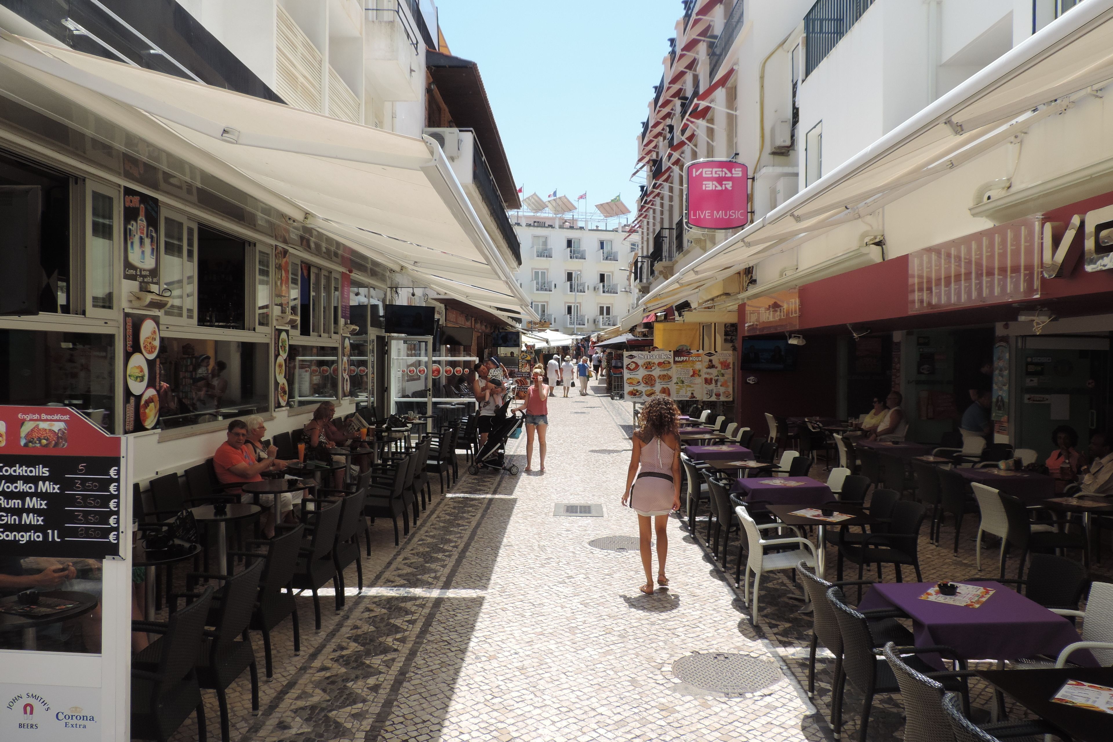 A narrow street with outdoor seating, cafes, and shops.