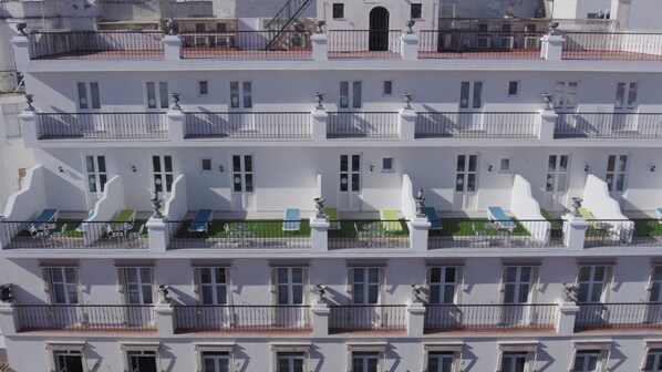 A multi-story hotel with balconies, each with a small table and chairs.