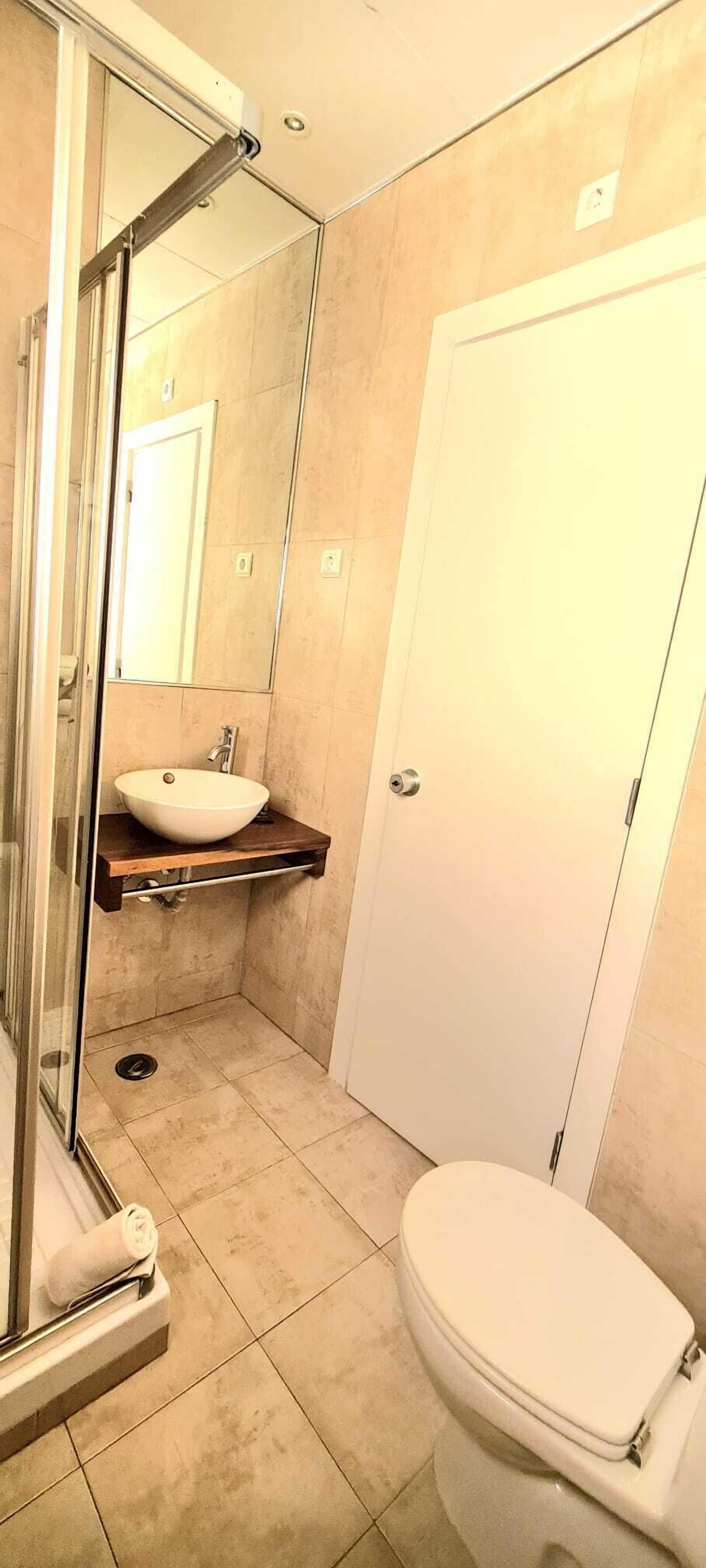 Een badkamer met een douchecabine van glas, een wastafel met spiegel, en een toilet.