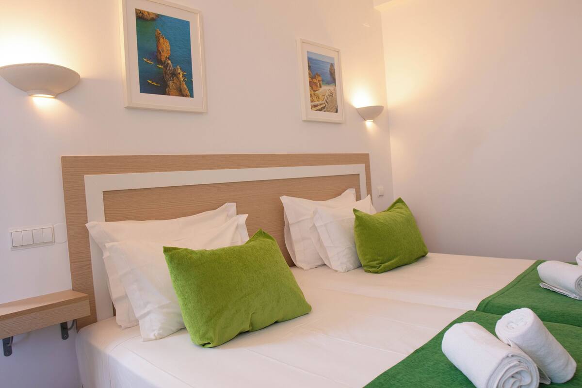 A hotel room with a large bed, two pillows, a nightstand, and two wall-mounted lights.
