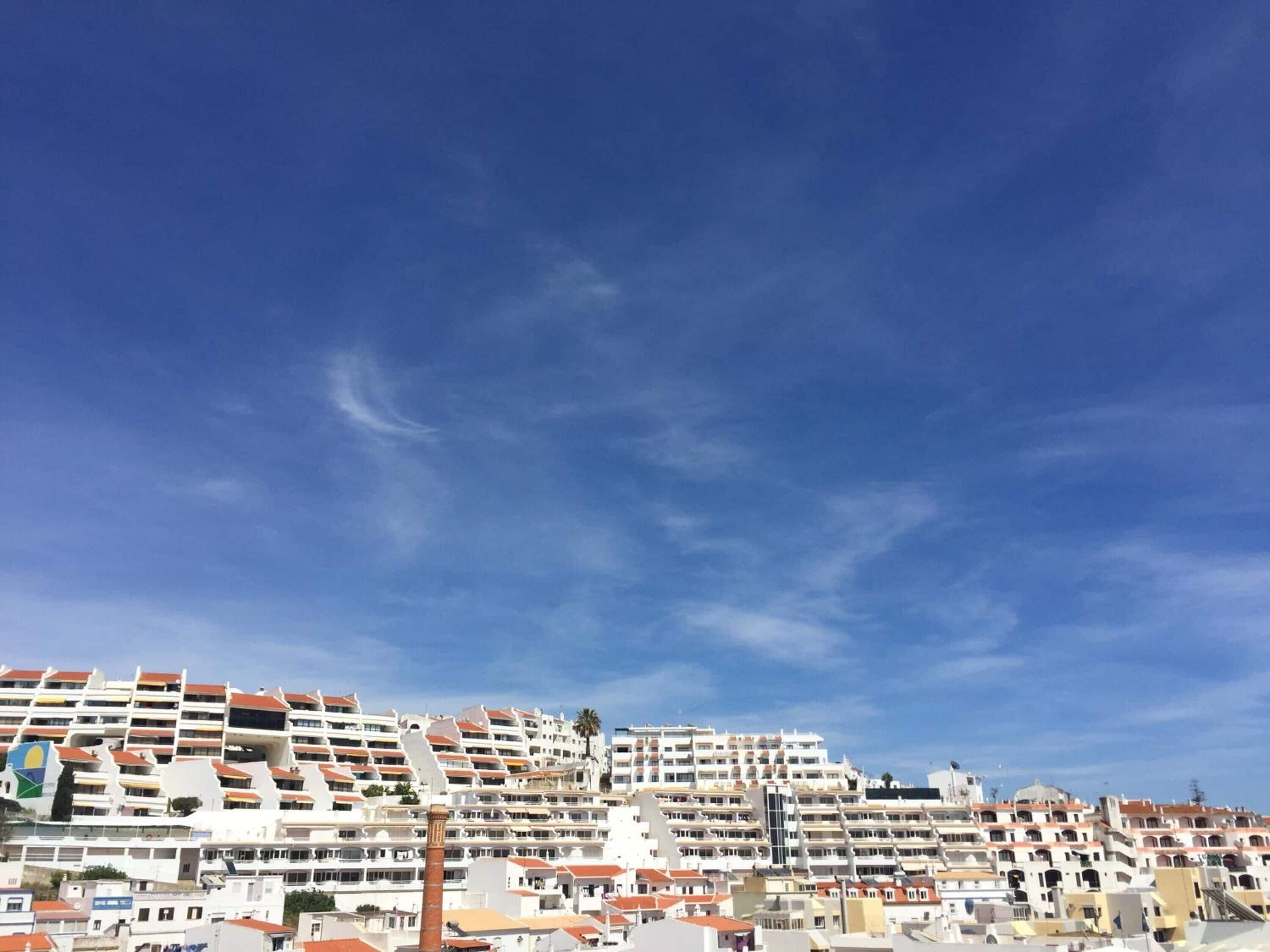 A coastal residential area with multi-story buildings, balconies, and a clear blue sky.