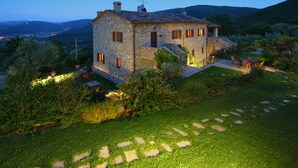 Una casa de piedra con un jardín cuidado, un patio con mobiliario exterior y vistas a las colinas circundantes.