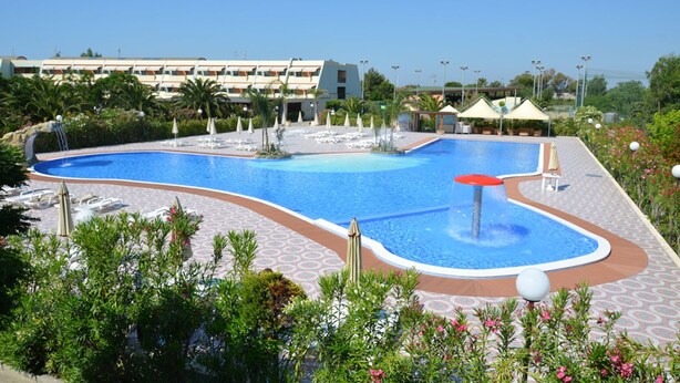 A large outdoor swimming pool with lounge chairs and umbrellas, surrounded by greenery and a hotel building in the background. - Alessidamo Club Metaponto (Bernalda)