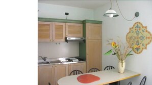 A kitchen with wooden cabinets, a stove, and a dining table with chairs. - Alessidamo Club Metaponto (Bernalda)