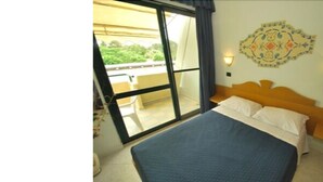 A bedroom with a bed, a window, a wall-mounted light fixture, and a decorative wall piece. - Alessidamo Club Metaponto (Bernalda)
