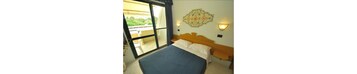 A bedroom with a bed, a window, a wall-mounted light fixture, and a decorative wall piece.
