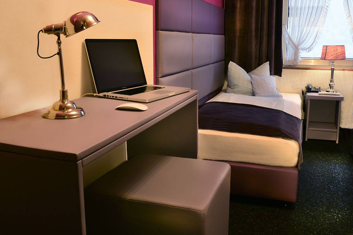A hotel room with a desk, laptop, bed, and bedside table.
