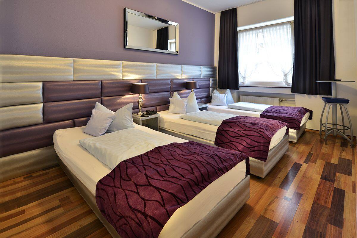 A hotel room with two beds, a large mirror, a window with curtains, and a wooden floor.