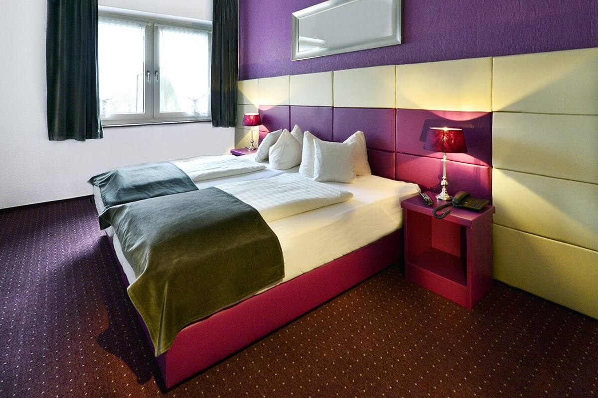 A hotel room with a bed, bedside tables, a window, and a mirror on the wall.