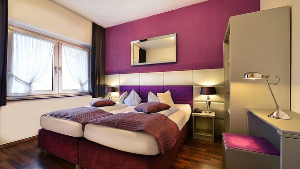 Una cama doble con cabecera, mesitas de noche con lámparas, un armario y una ventana con cortinas.