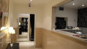 Una habitación de hotel con un espejo grande, un escritorio con lámpara, televisor y un reloj en la pared.