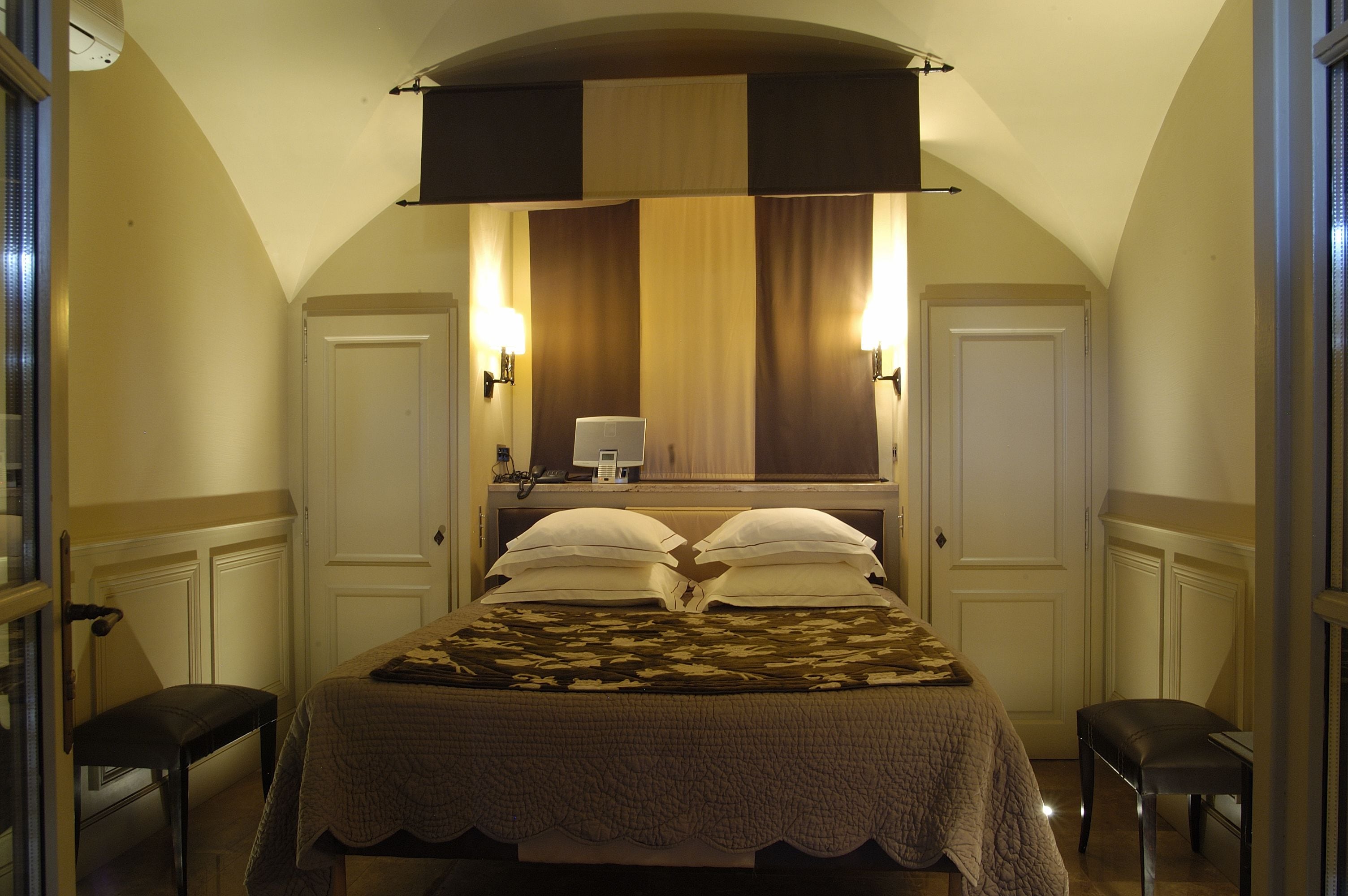 Habitación de hotel con cama, dos mesitas de noche, un escritorio con lámpara y un ventanal con cortinas.
