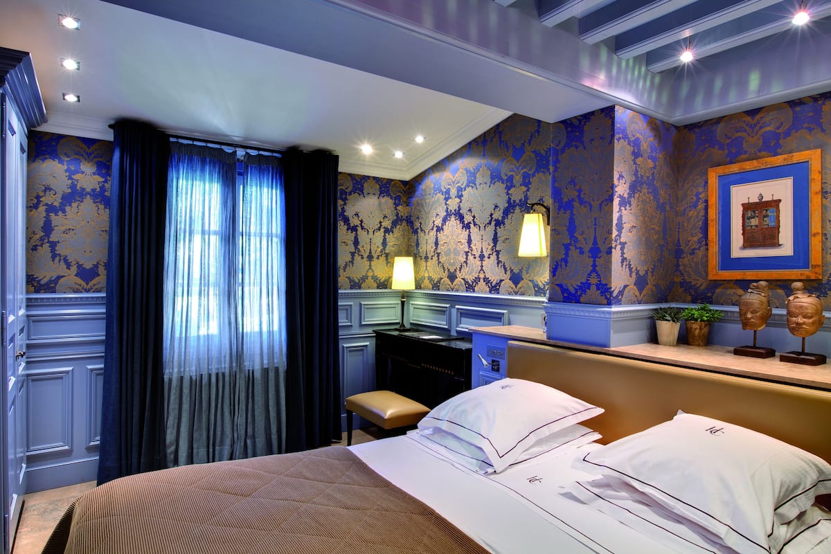A hotel room with a bed, a desk, a chair, and a small table with decorative items.