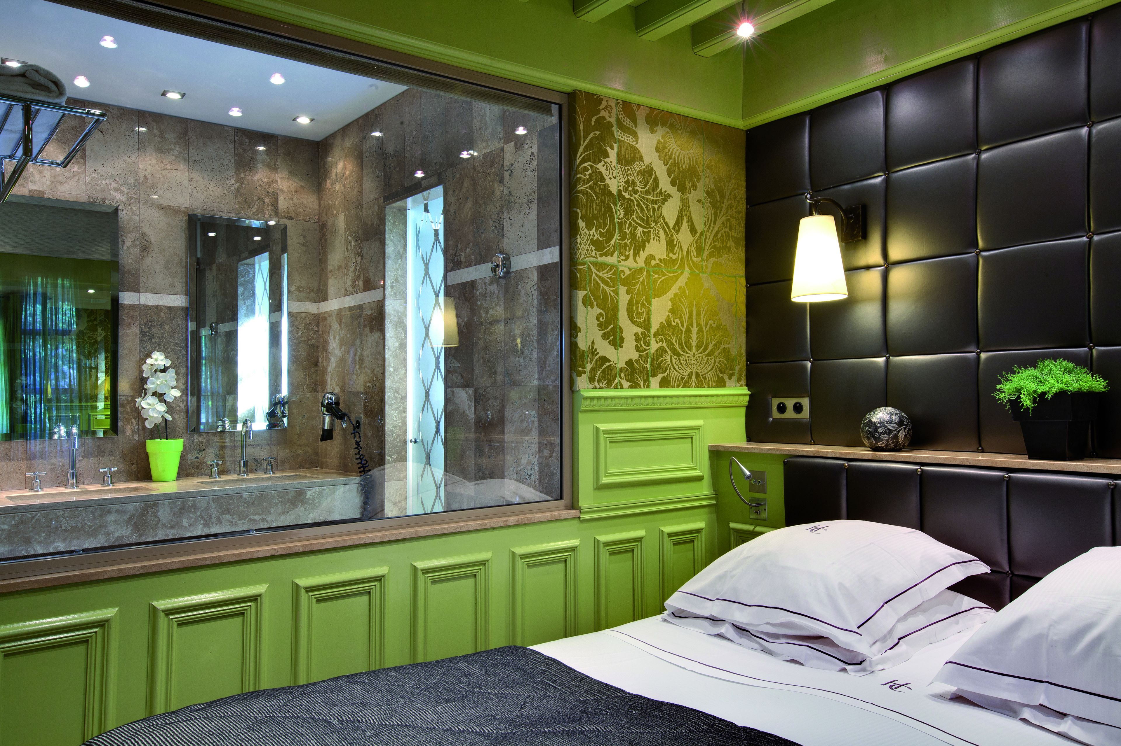 Un baño moderno con un espejo grande, paredes verdes y un cabecero acolchado negro.