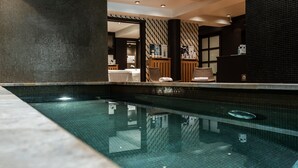 Piscina interior moderna con agua cristalina, rodeada de paredes de azulejos oscuros y un mostrador de recepción de madera.