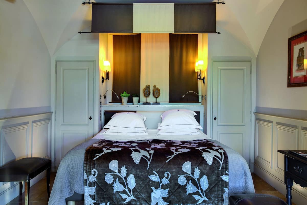 A hotel room with a bed, two bedside lamps, a nightstand, a bench, and a mirror above the bed.