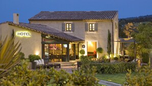 Un hotel con un patio, mobiliario exterior y una entrada bien iluminada.