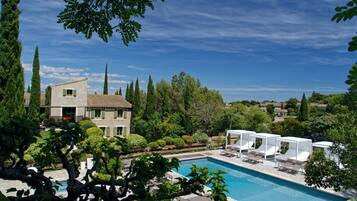 A pool area with lounge chairs, a building with a tiled roof, and surrounding greenery.