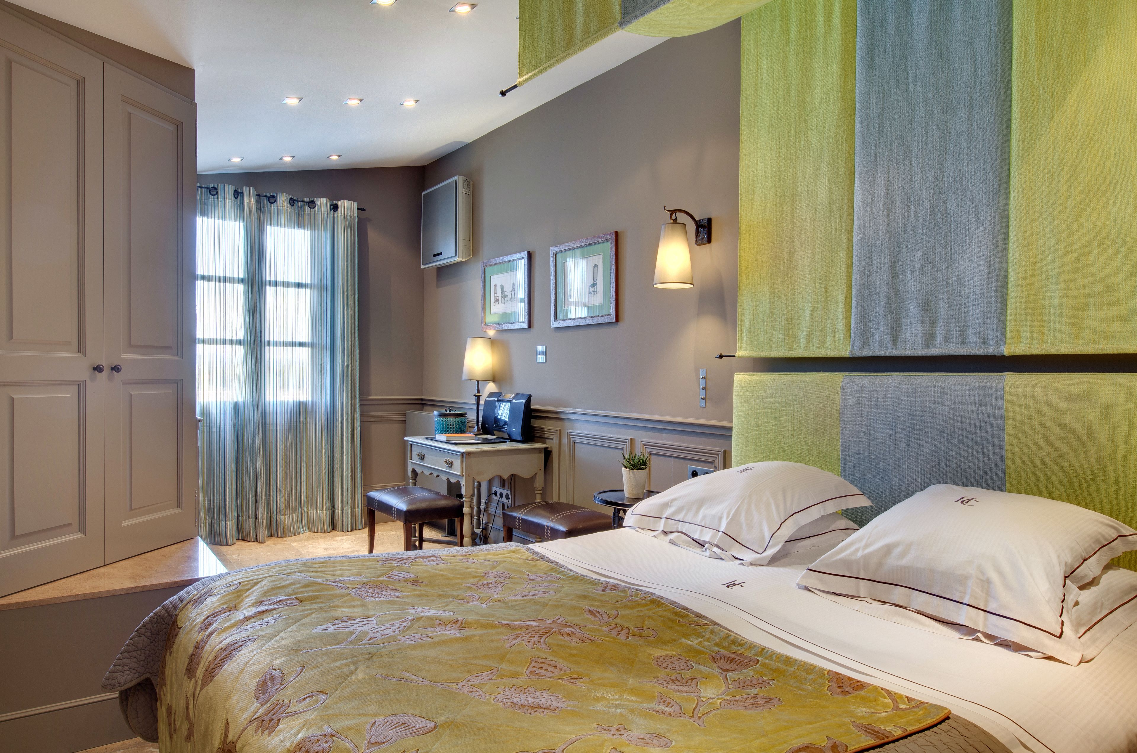 A hotel room with a bed, a desk, a chair, a lamp, and a window with curtains.