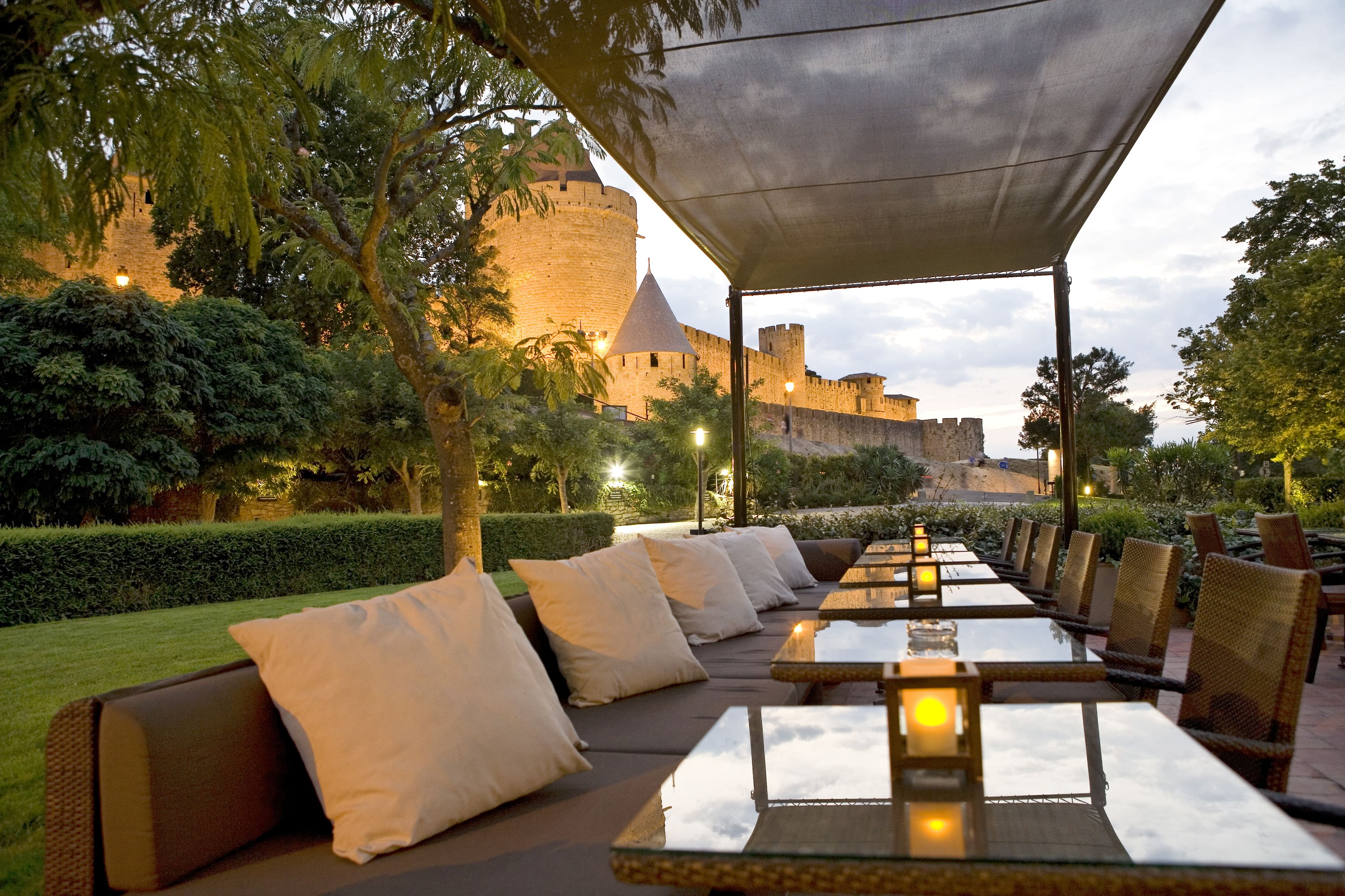 An outdoor dining area with tables and chairs, a canopy, and a castle in the background.