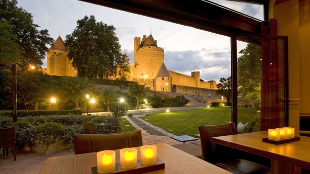 Un restaurante con vistas a un castillo, mesas al aire libre y velas sobre la mesa.