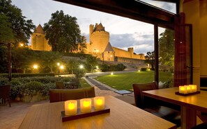 A restaurant with a view of a castle, outdoor seating, and candles on the table. - Hôtel du Château & Spa Gemology (Carcassonne)