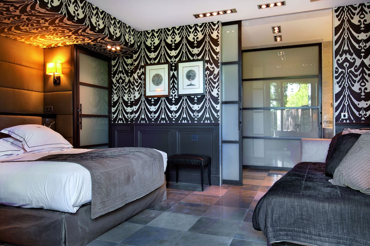 A modern hotel room with two beds, a large window, and patterned wallpaper.