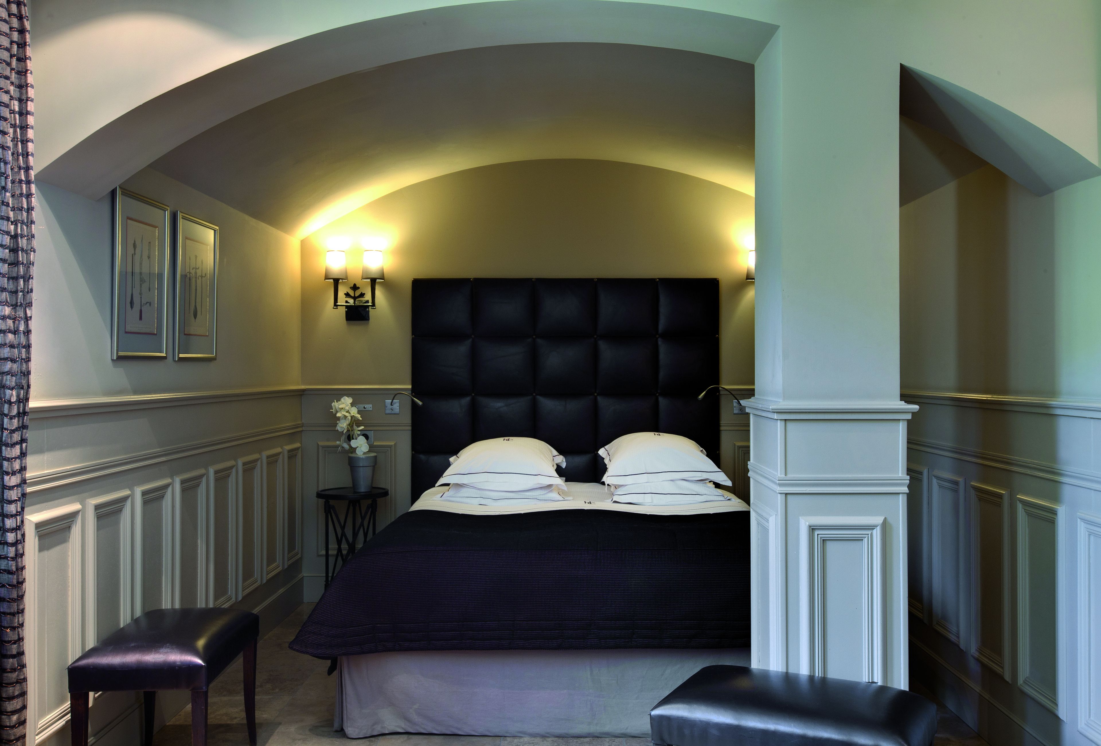 A bedroom with a large bed, two bedside tables, a small table with a plant, and a bench.