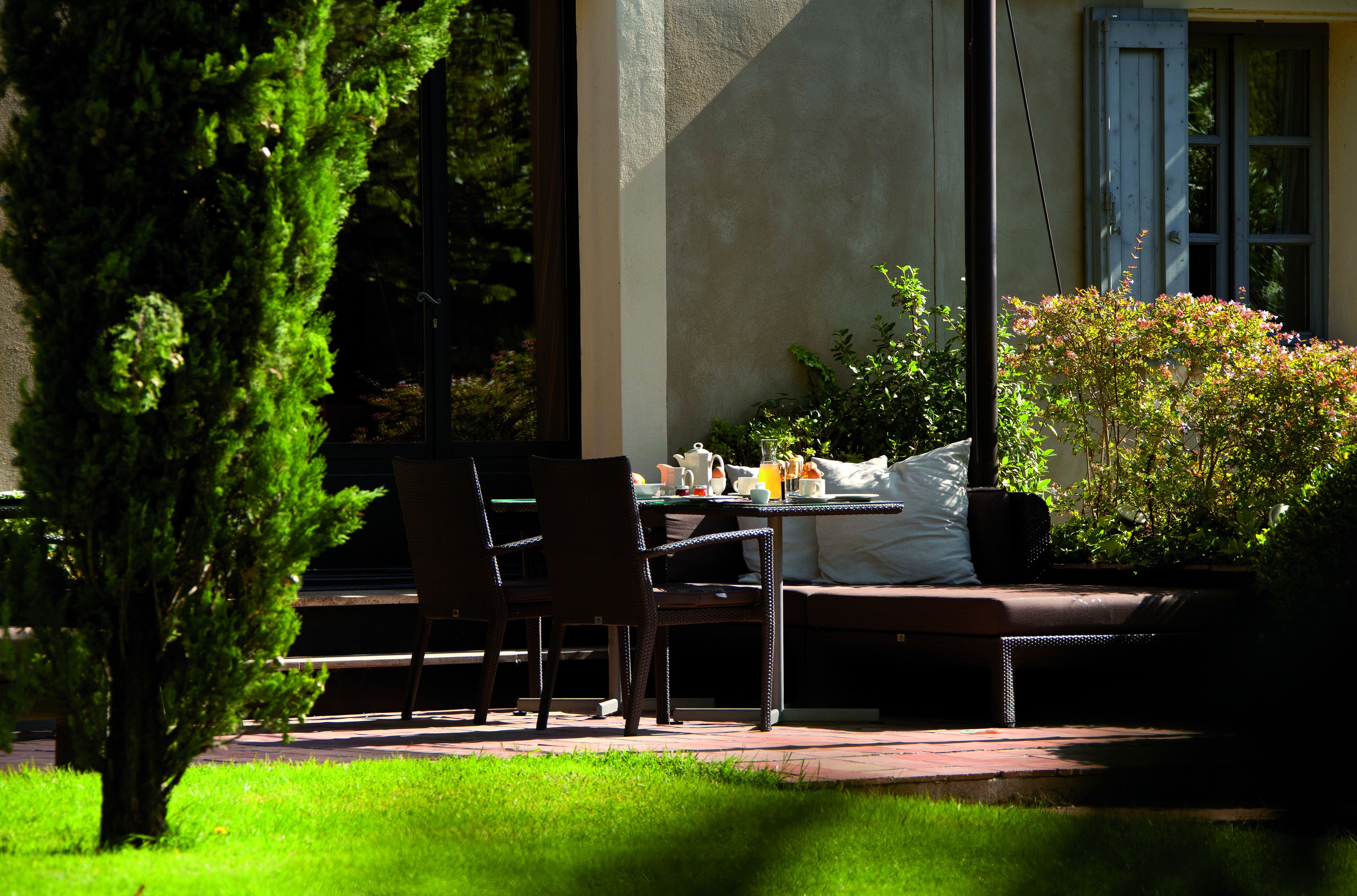 Un espace extérieur aménagé avec une table dressée pour le petit-déjeuner, entouré de chaises et d’un banc.