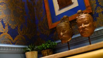 A room with ornate blue wallpaper and a wooden shelf displaying two wooden masks.
