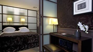 Habitación de hotel con cama, dos lámparas de noche, escritorio con computadora, pequeño banco y un cuadro en la pared.