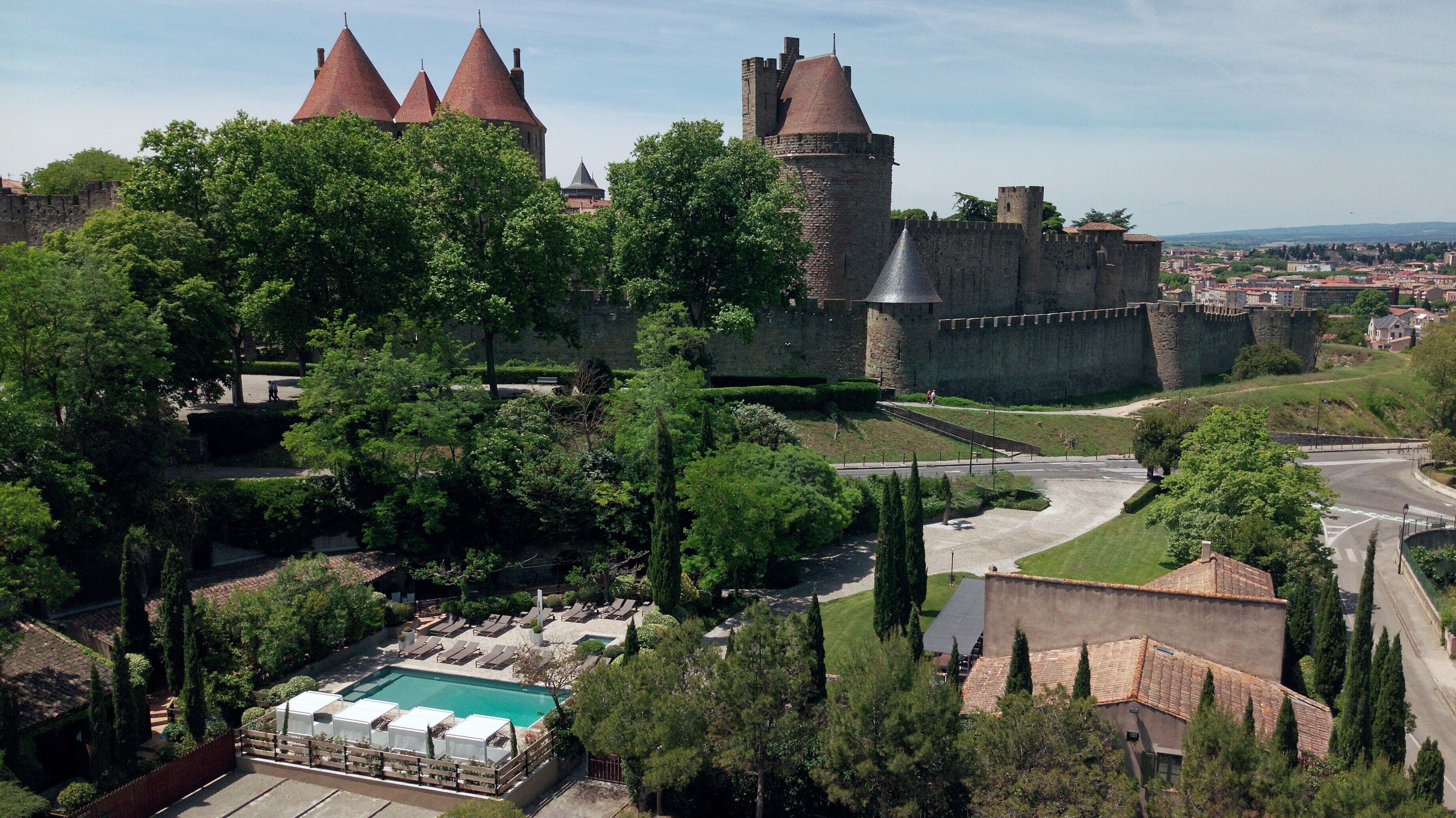 A castle with multiple towers, a swimming pool, and a surrounding park.