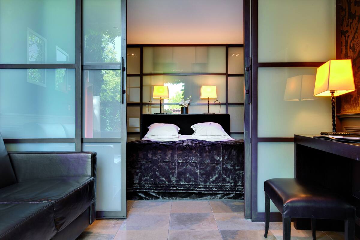 A modern hotel room with a large bed, two bedside lamps, a desk, and a chair.