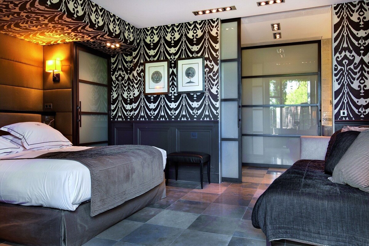 Habitación de hotel con dos camas, un sofá, un ventanal grande y papel tapiz estampado.