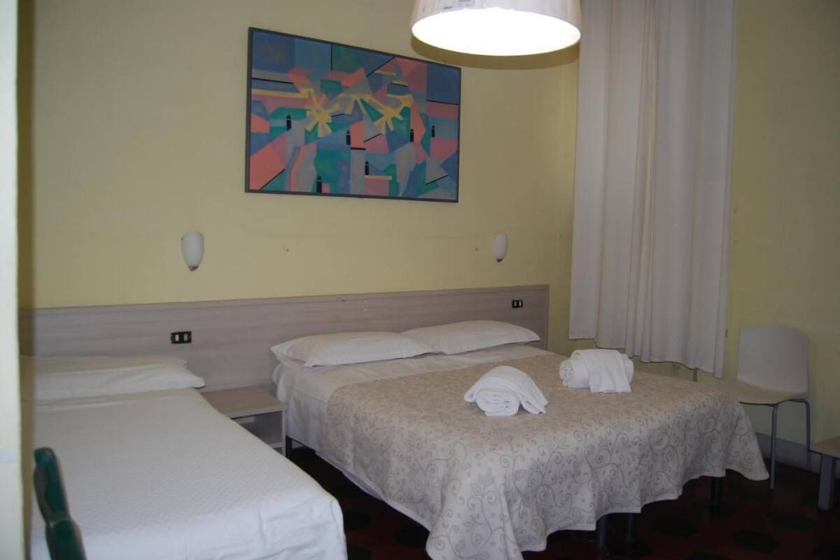 A hotel room with two beds, a painting on the wall, and a chair.
