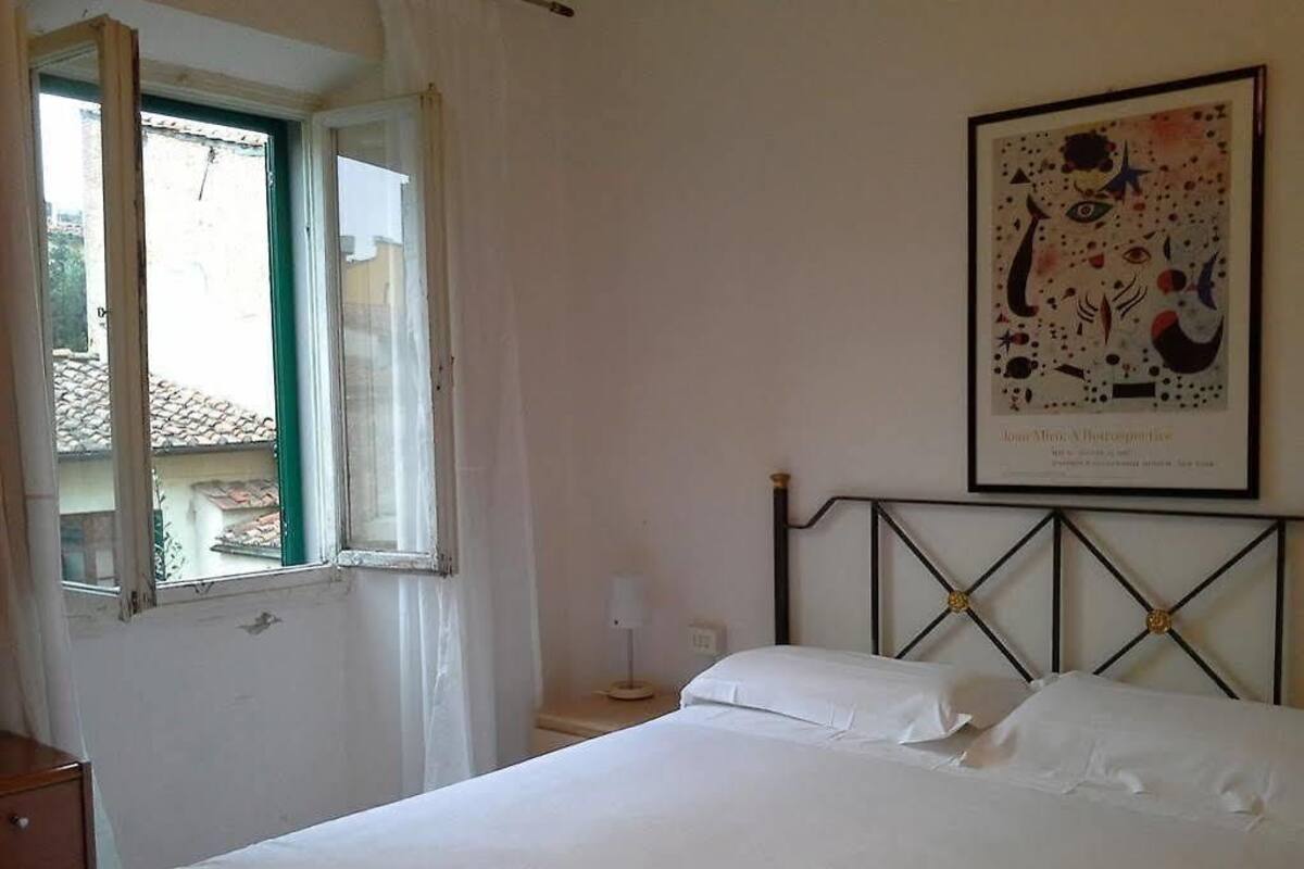 A bedroom with a bed, a window, a nightstand, and a framed picture on the wall.