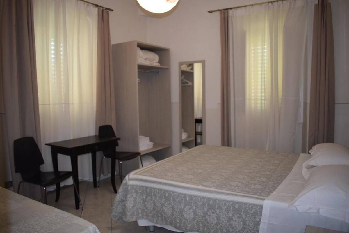 A hotel room with a bed, a desk, a chair, a wardrobe, and a mirror.