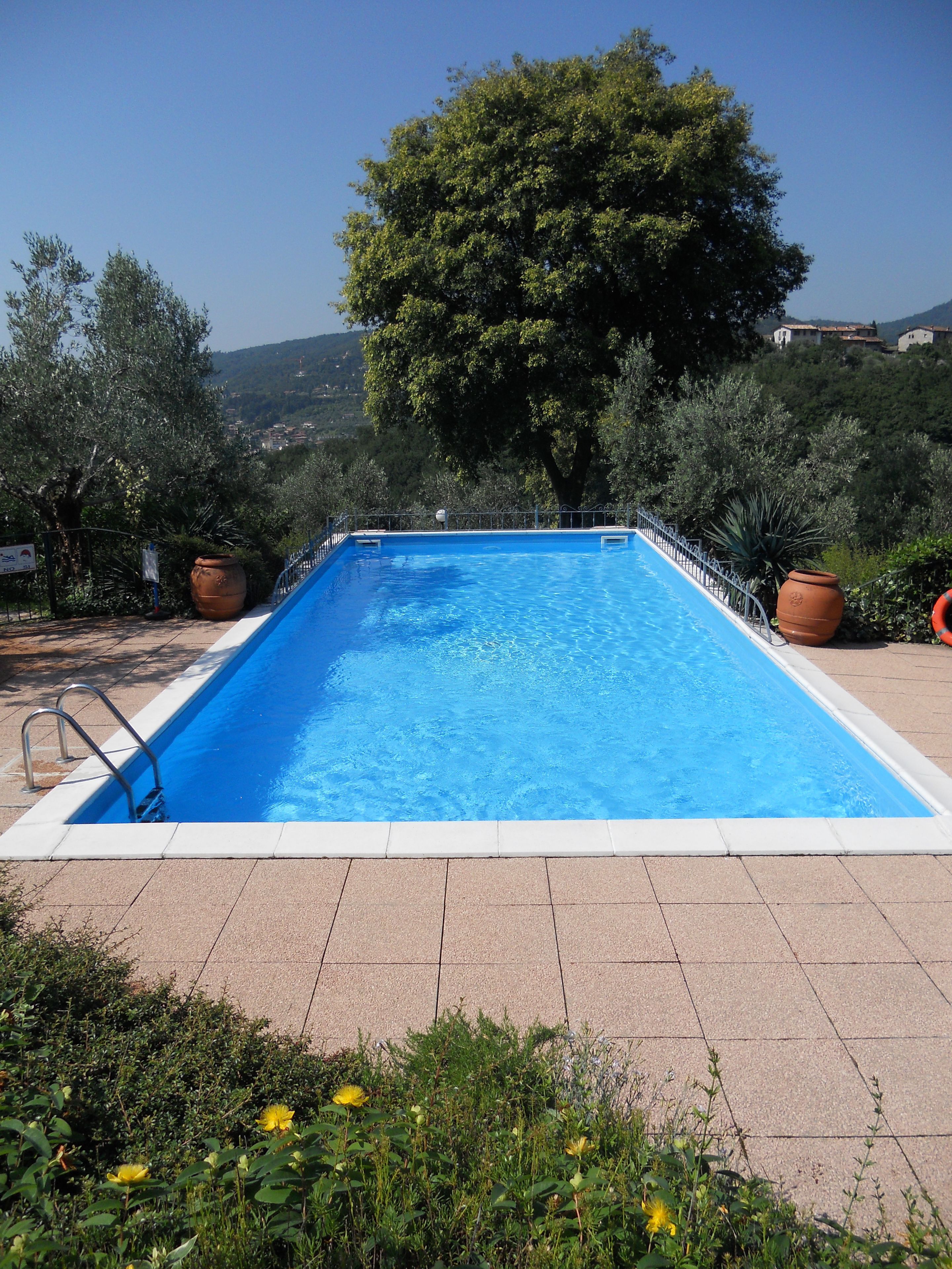 Une piscine rectangulaire bordée de blanc, entourée d’une clôture en métal et située sur une terrasse carrelée.
