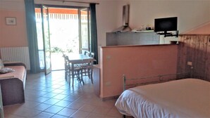 Il s’agit d’une pièce de taille modeste, comprenant un lit, une petite table et une chaise. Un téléviseur est fixé au mur et une fenêtre laisse entrer la lumière naturelle.